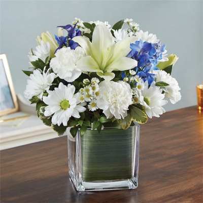White lilies and daisies with blue flowers in a square glass vase