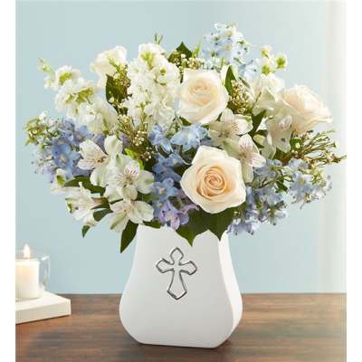 White and pale blue floral arrangement in a white vase with a cross