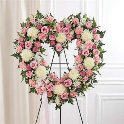 Heart-shaped floral wreath with pink roses and white blooms on an easel