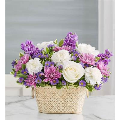 Purple, pink, and white flowers arranged in a decorative cream container