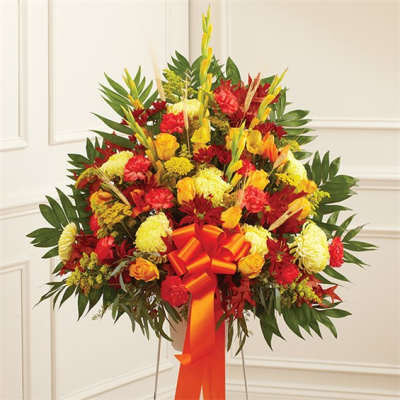 Large red and yellow floral standing arrangement with a ribbon bow