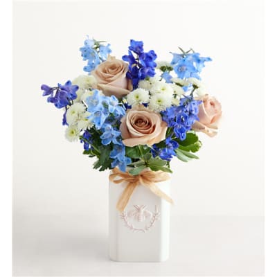 Bouquet of peach roses, blue flowers, and white blooms in a white vase