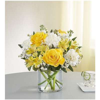 Yellow roses and white flowers arranged in a clear glass vase