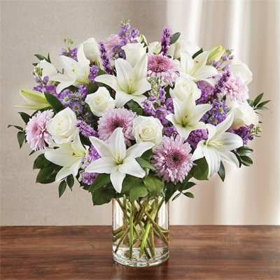 Bouquet of white lilies, roses, and purple flowers in a clear glass vase