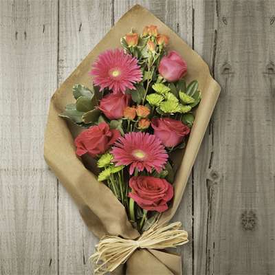 Bouquet of hot pink roses and gerbera daisies wrapped in brown paper