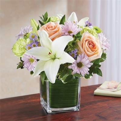 Bouquet of white lilies, peach roses, and lavender daisies in a square glass vase