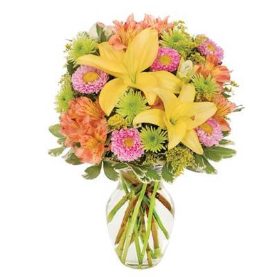 Mixed bouquet of yellow lilies, pink daisies, and orange flowers in a clear glass vase