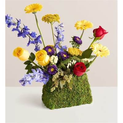 Mixed bouquet of roses, daisies, and blue flowers in a moss-covered container