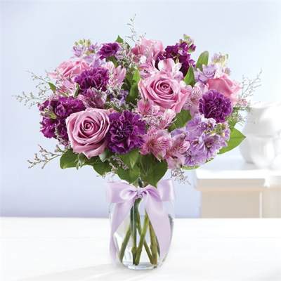 Pink and purple bouquet in a clear glass vase with a lavender ribbon