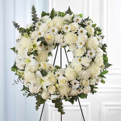 White floral wreath on a black stand with roses and lilies
