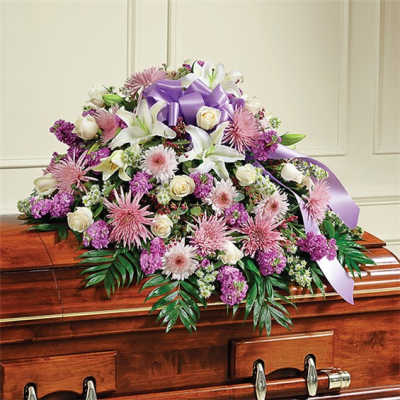 Lavender and white floral spray on a wooden casket with a purple ribbon