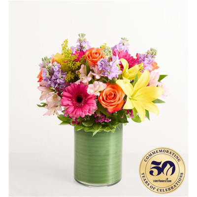 Colorful mixed bouquet in a green glass vase with roses, lilies, and daisies