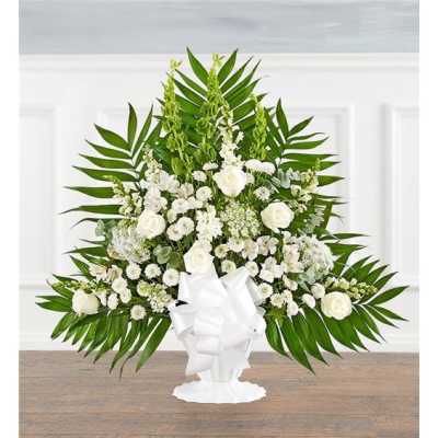White floral standing arrangement with palm fronds and a white bow in a pedestal vase