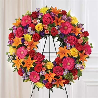 Colorful floral wreath on a black stand with roses, lilies, and daisies