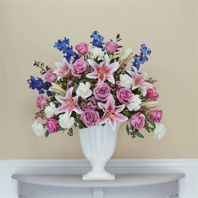 Pink roses and lilies arranged in a white urn vase