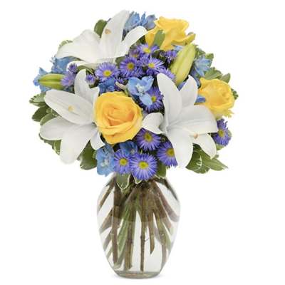 Bouquet of white lilies, yellow roses, and purple daisies in a glass vase