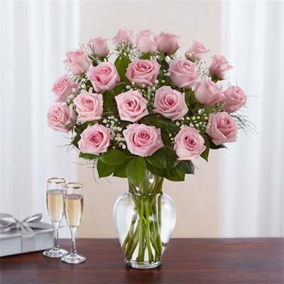 Pink roses in a clear glass vase with two champagne flutes and a gift box
