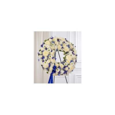 Round floral wreath of white and blue flowers on a stand with a blue ribbon