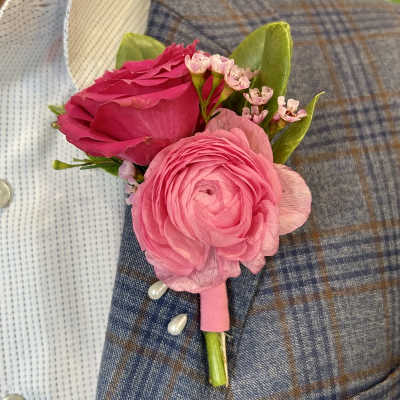 Pink ranunculus and rose boutonniere with pearl pins on a blue plaid suit lapel