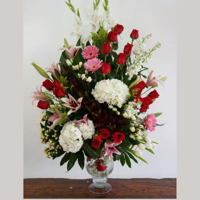 Tall mixed arrangement of red roses, white hydrangeas, pink lilies and gerberas in a clear glass vase