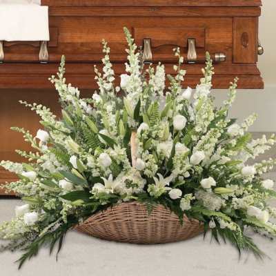 White floral spray in a wicker basket in front of a wooden casket