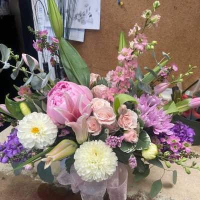 Pink and purple mixed flower arrangement with lilies and roses in a ribboned base