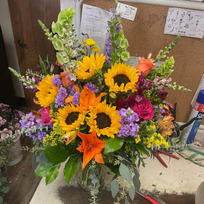 Bright mixed bouquet with sunflowers, lilies, roses, and purple spikes in a glass vase