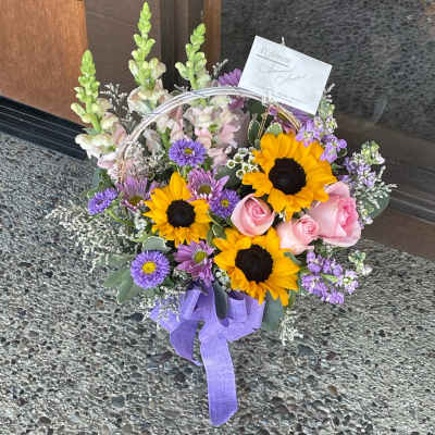Basket arrangement with sunflowers, pink roses, and purple flowers