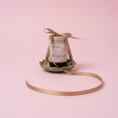 Tea bottle tied with a gold ribbon on a small dish against a pink background
