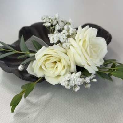 White rose boutonniere with small white filler flowers and dark green leaves