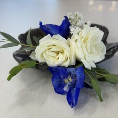 Small floral corsage with white roses and blue flowers on a dark base