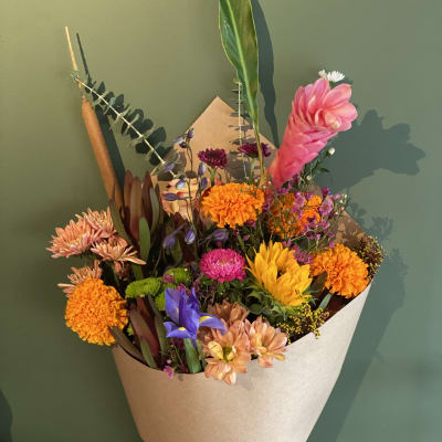 Hand-tied bouquet of mixed pink, orange, yellow, and purple flowers in kraft paper