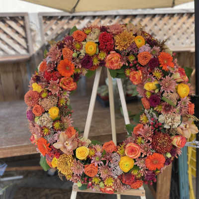 Circular floral wreath on an easel with orange, pink, yellow, and purple blooms