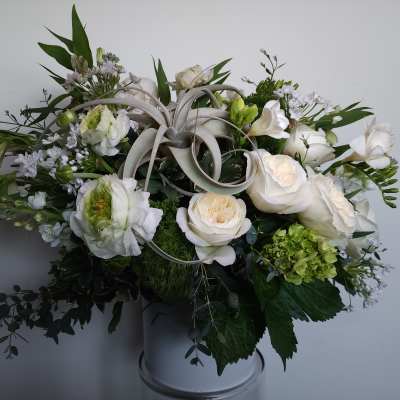 White floral arrangement in a vase with green accents and curled ribbon loops