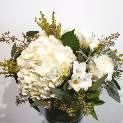 White hydrangeas and roses in a glass vase with mixed greenery
