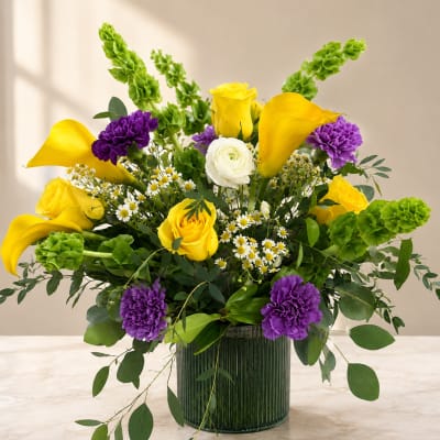 Bouquet of yellow roses, purple carnations, and white daisies in a glass vase