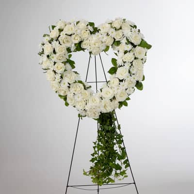 White rose heart wreath on a black stand with trailing greenery