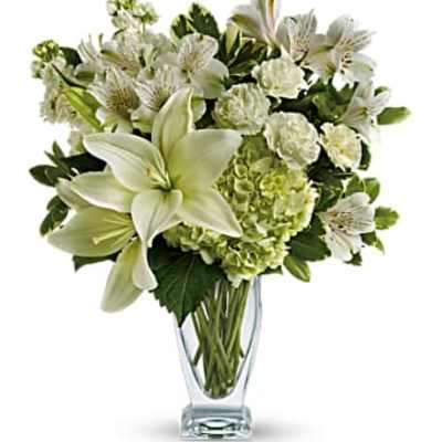White lilies and mixed white flowers in a clear glass vase