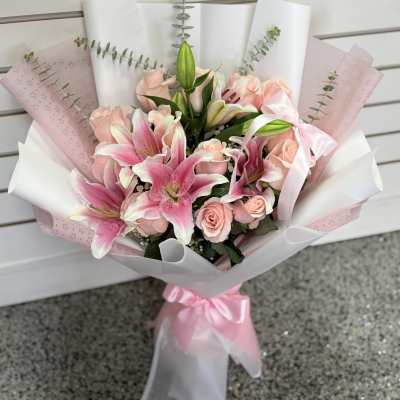 Pink lilies and roses wrapped in white and pink paper with a ribbon