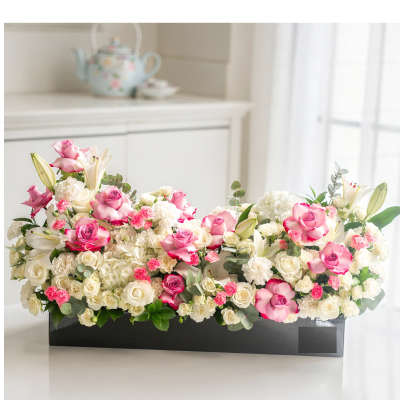 Pink and white roses with lilies arranged in a black rectangular box