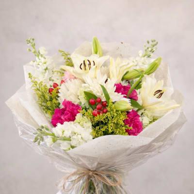 Bouquet of white lilies, pink carnations, and white chrysanthemums wrapped in paper