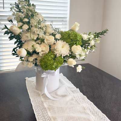 White floral arrangement in a white hatbox with green hydrangeas and roses