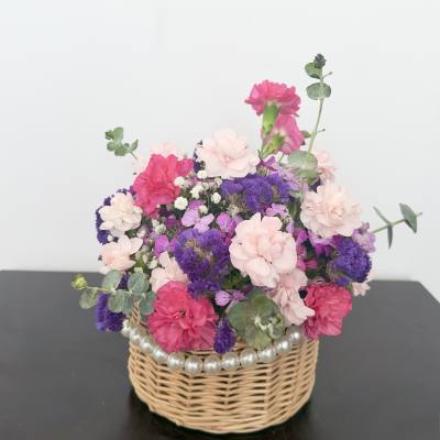 Pink and purple flower arrangement in a wicker basket with pearl trim