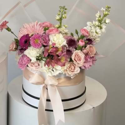 Pink and white mixed flower arrangement in a round hat box with ribbon