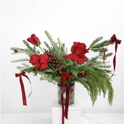 Red roses in a glass vase with pine branches and burgundy ribbons