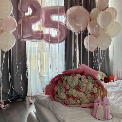 Pink and white balloons with a large 25 balloon above a bouquet on a bed