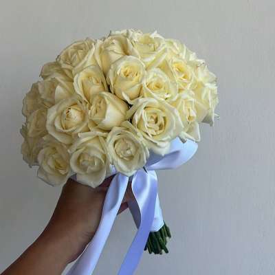 Handheld bouquet of cream roses tied with a pale ribbon