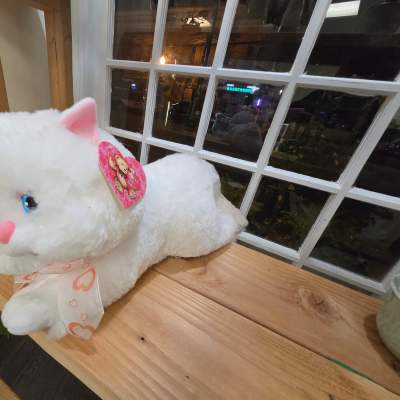 White plush cat with pink ears and a ribbon on a wooden shelf
