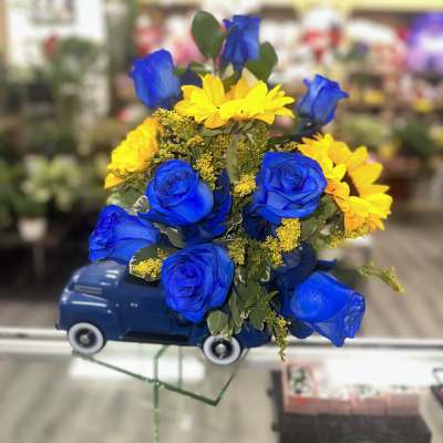 Blue roses and yellow daisies arranged in a blue ceramic truck container