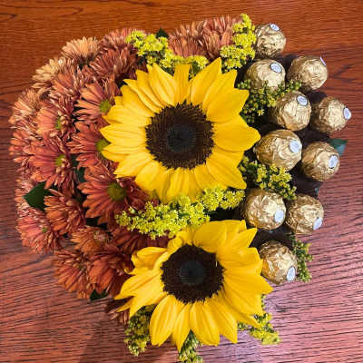 Low arrangement of yellow sunflowers, rust mums, and gold-wrapped chocolates.